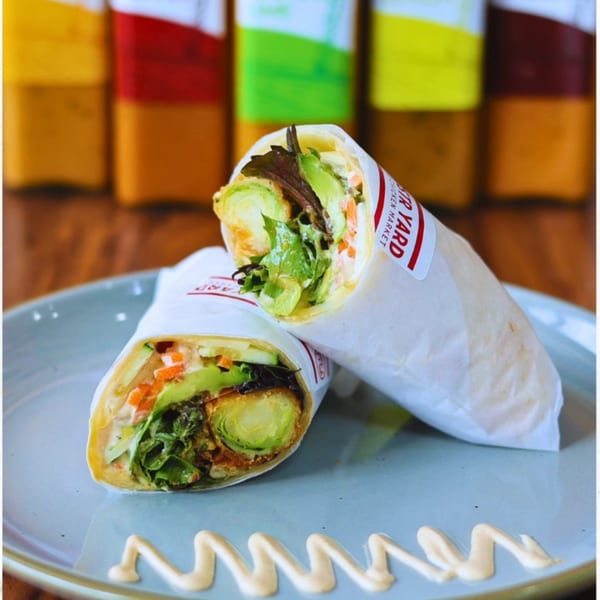 Two Roostr Yard wraps, filled with grilled chicken, avocado, and brussels sprouts, on a blue plate.