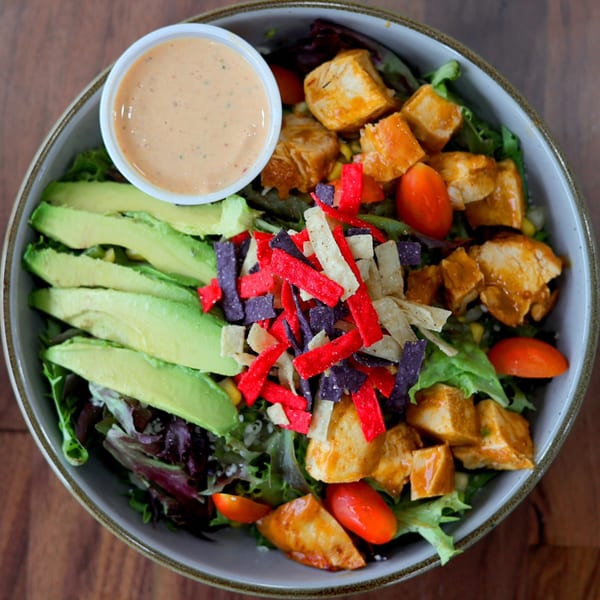 Overhead view of a Roostr Yard grilled chicken salad with avocado, tomatoes, and tortilla strips.