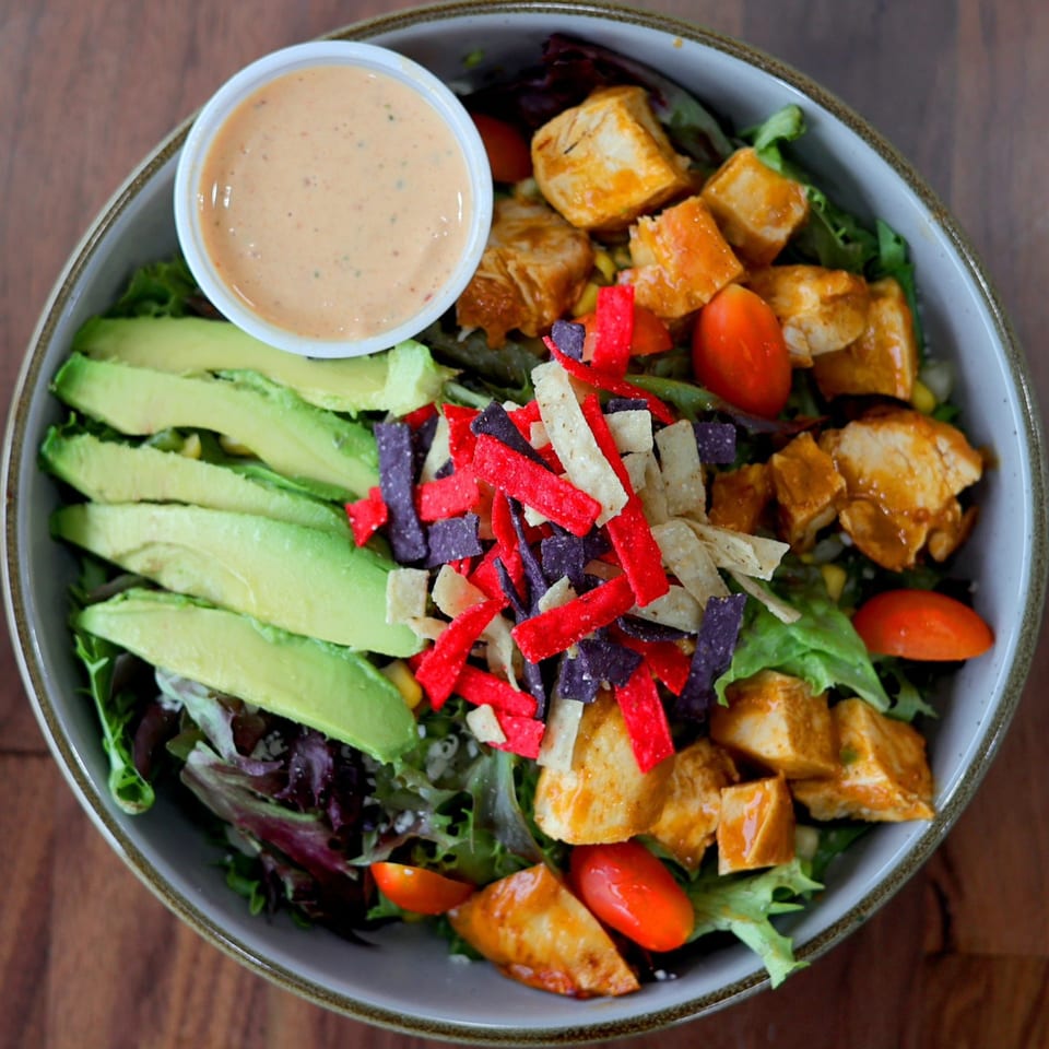 Overhead view of a Roostr Yard grilled chicken salad with avocado, tomatoes, and tortilla strips.