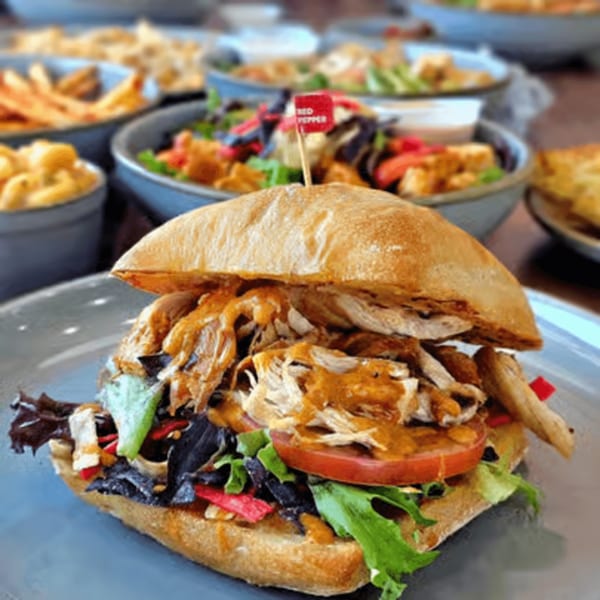 Roostr Yard's grilled chicken sandwich with lettuce, tomato, and sauce, surrounded by sides.