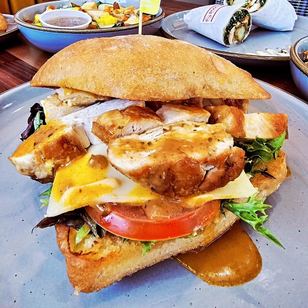 A Roostr Yard grilled chicken sandwich with cheese, tomato, and sauce on a ciabatta bun.