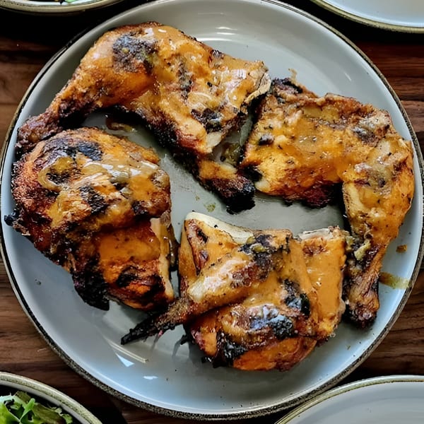 Four pieces of Roostr Yard's grilled chicken, glistening with sauce, on a light grey plate.