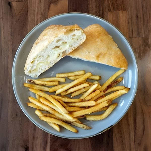 A light blue plate holds golden french fries and two halves of a fluffy white bread roll.